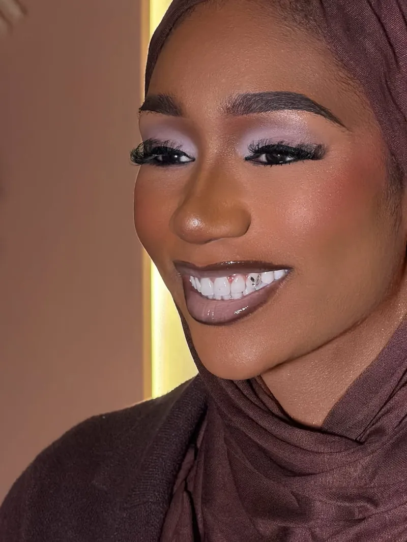 Smiling with lilac eyeshadow, full lashes and a glossy mauve lip